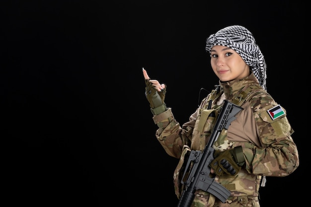 Mujer soldado en uniforme militar con rifle en la pared negra