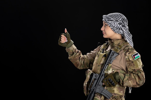 Foto gratuita mujer soldado en uniforme militar con rifle en la pared negra