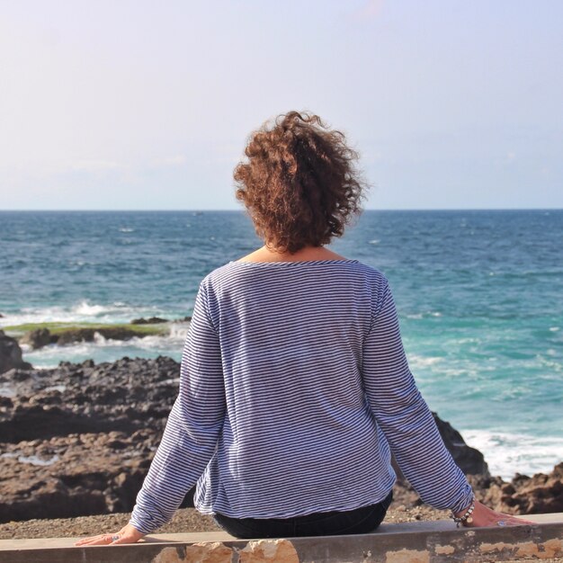 Mujer solitaria sentada sobre una roca y disfrutando de la hermosa vista del mar