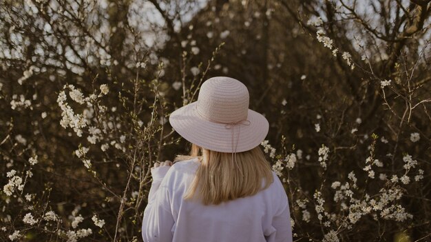 Mujer con sombrero cerca del árbol con flores blancas