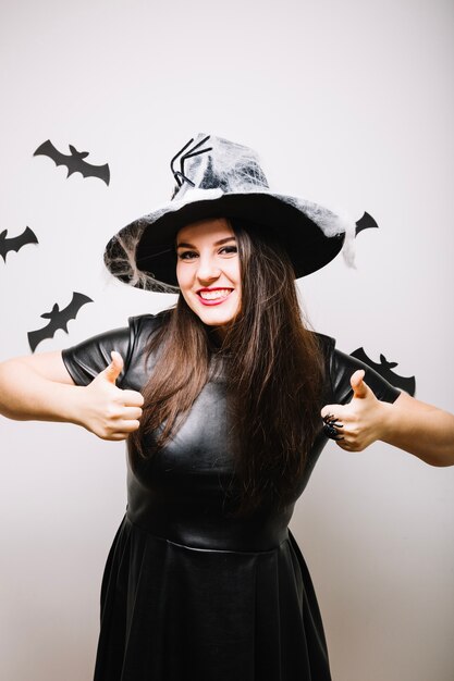 Mujer en el sombrero de Halloween con los pulgares para arriba