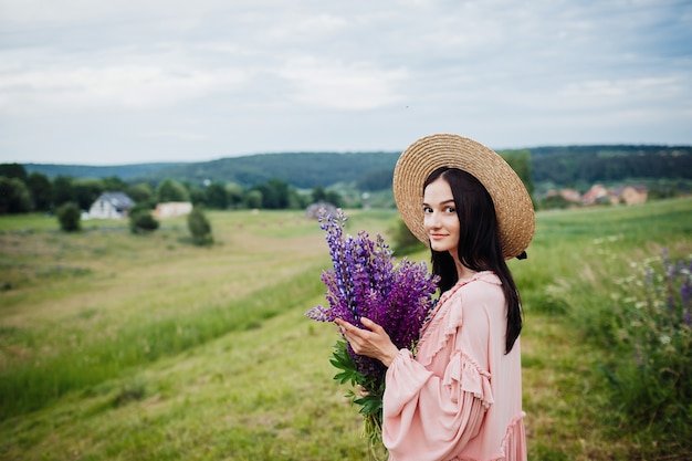 Mujer en sombrero de heno posa con ramo de lavanda en el campo