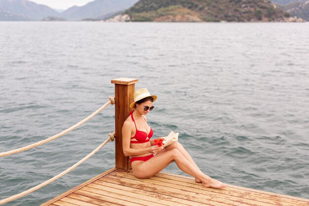 Mujer con sombrero y libro de lectura en el muelle