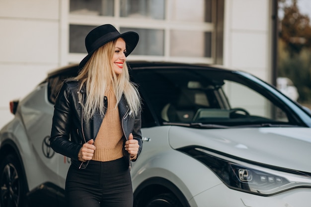 Mujer con sombrero negro de pie junto a su nuevo coche blanco