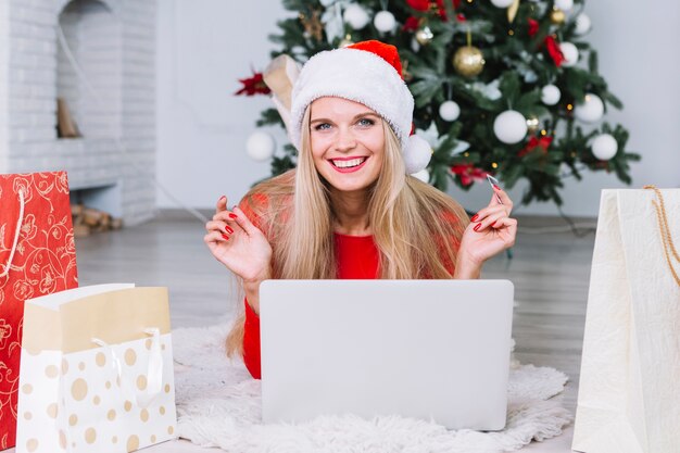 Mujer en el sombrero de Papá Noel que miente con la computadora portátil