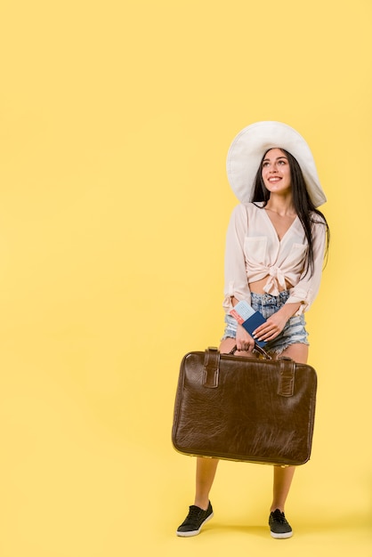 Mujer en sombrero de pie y sosteniendo la maleta