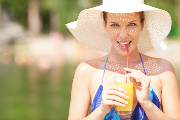 Mujer con un sombrero que bebe un jugo