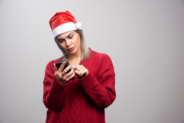 Mujer con sombrero de Santa mirando celular.