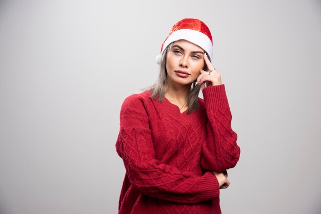 Mujer con sombrero de Santa pensando en fondo gris.