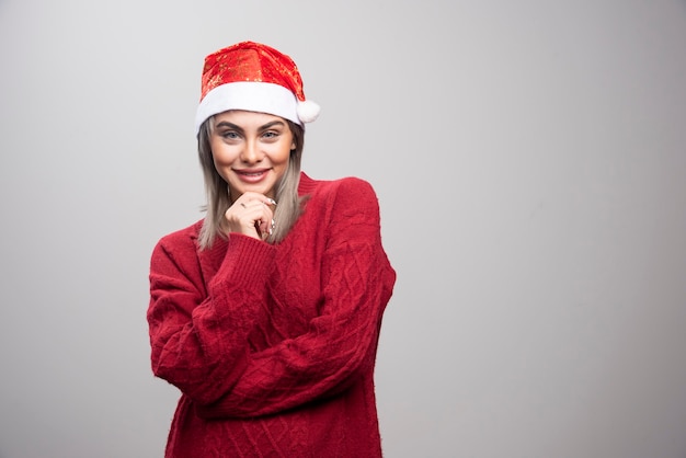 Mujer con sombrero de Santa de pie felizmente sobre fondo gris.