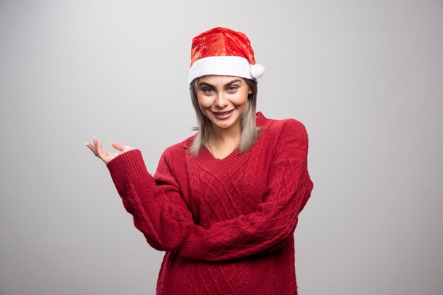 Mujer con sombrero de Santa de pie felizmente sobre fondo gris.