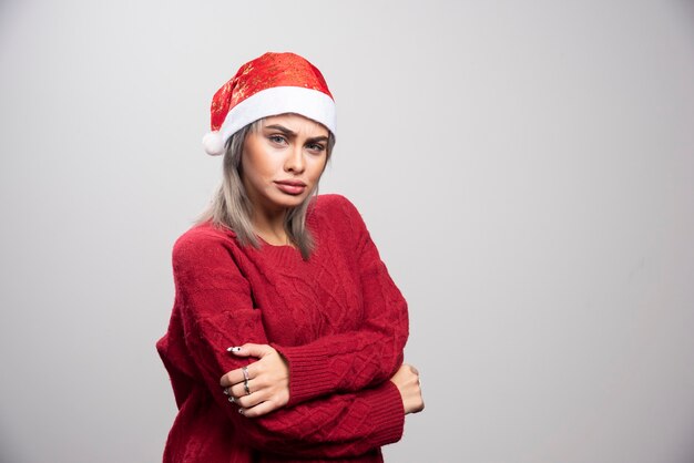 Mujer con sombrero de Santa posando sobre fondo gris.