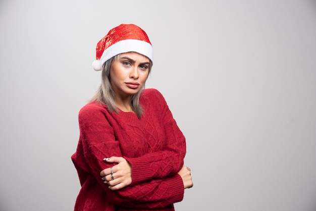 Mujer con sombrero de Santa posando sobre fondo gris.