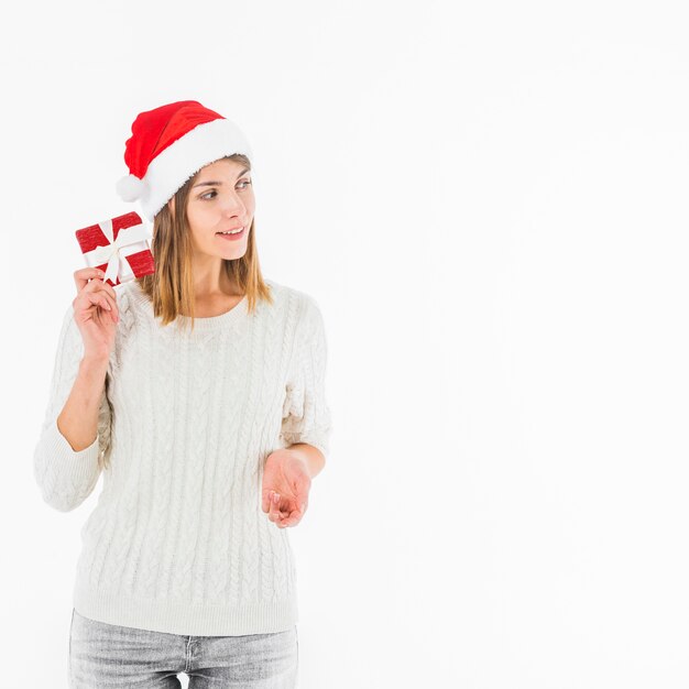 Mujer con sombrero de Santa sosteniendo una caja de regalo roja cerca de la oreja