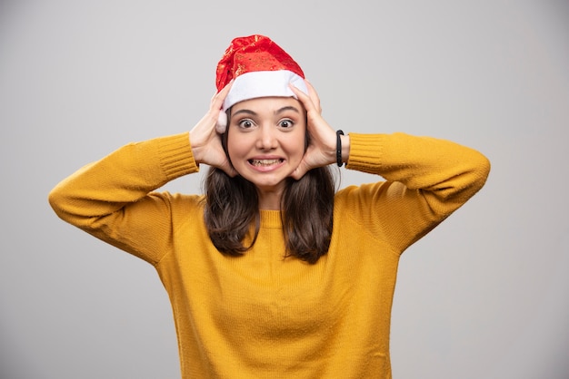 Mujer con sombrero de Santa sosteniendo su rostro en la pared gris.