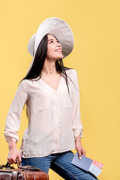 Mujer en sombrero sonriendo y sosteniendo boletos y maleta