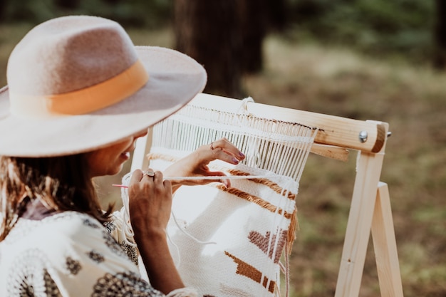 Foto gratuita mujer con sombrero y tejiendo una estera en un telar casero en el patio trasero