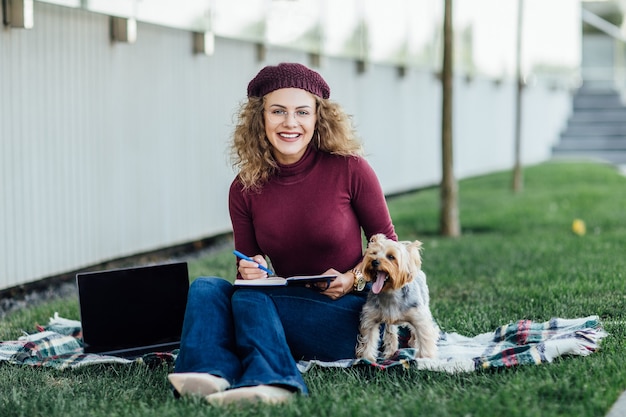 Mujer con un sombrero violeta en un picnic en el bosque, junto a ella en la manta un pequeño perro Yorkshire Terrier, la luz del sol, la saturación de colores brillantes, la unidad con la naturaleza.