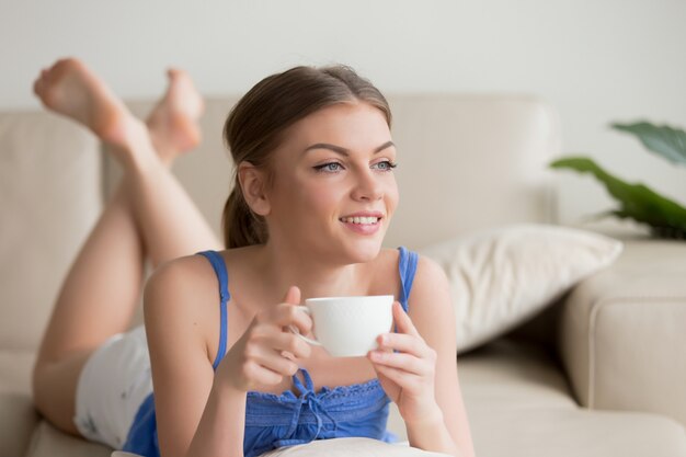 Mujer soñadora descansando en un cómodo sofá, disfrutando de una taza de café.