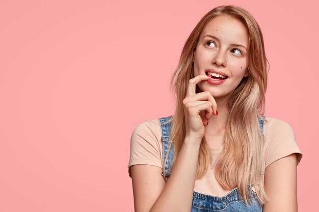 Mujer soñadora con expresión pensativa, mira hacia otro lado, mantiene la mano cerca de la cara, piensa en algo agradable