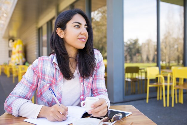 Mujer soñadora que hace notas en café al aire libre