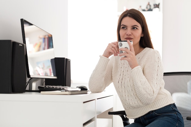 Mujer soñadora con taza en la oficina en casa