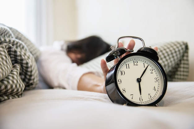 Mujer soñolienta alcanzando sosteniendo el despertador