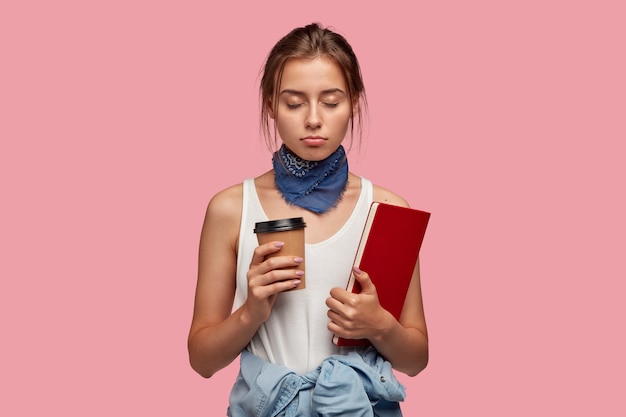 Mujer soñolienta con mirada triste, sostiene el libro de texto, mantiene los ojos cerrados porque quiere descansar