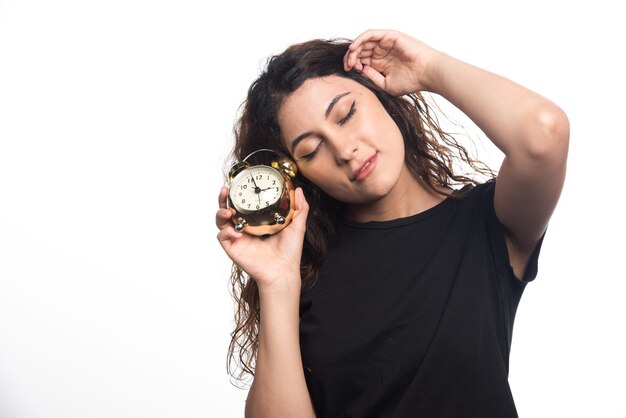 Mujer soñolienta con reloj sosteniendo su cabeza sobre fondo blanco.