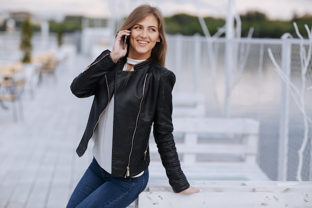 Mujer sonriendo apoyada en una tabla de madera blanca hablando por teléfono