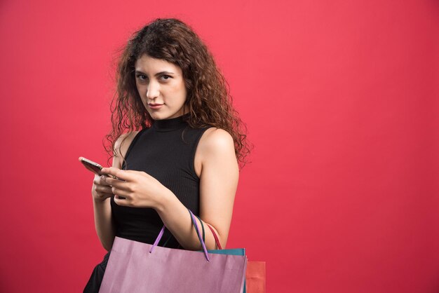 Mujer sonriendo con bolsas de ropa nueva y teléfono en rojo