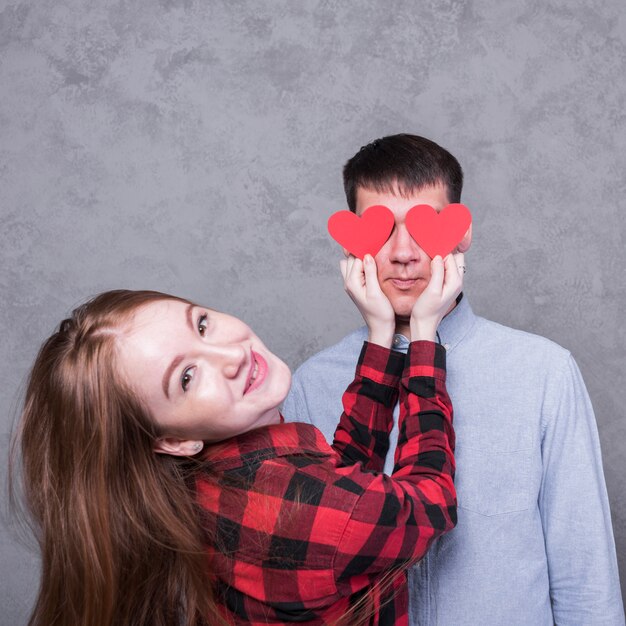 Mujer sonriendo y cubriendo ojos de hombre con corazones de papel