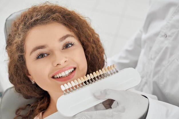Mujer sonriendo mientras el dentista masculino mantiene la gama de colores de los dientes