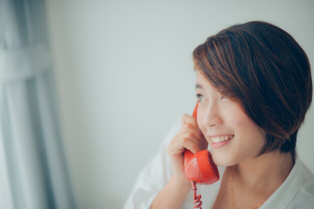 Mujer sonriendo mientras habla por un teléfono rojo de cerca