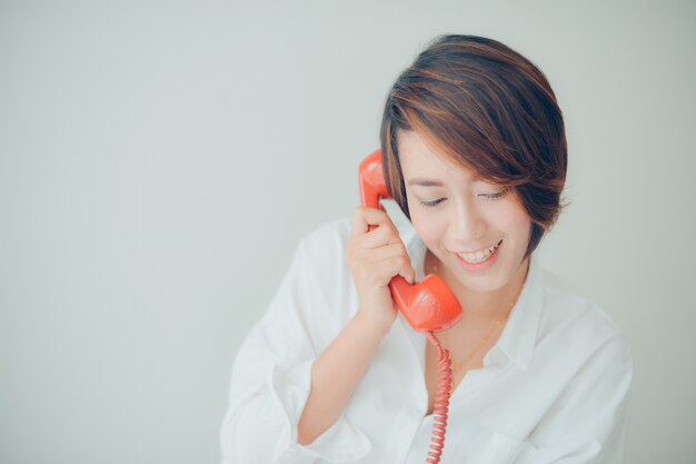 Mujer sonriendo mientras habla por un teléfono rojo