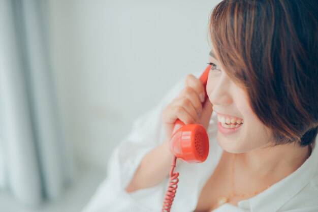 Mujer sonriendo mientras habla por un teléfono rojo