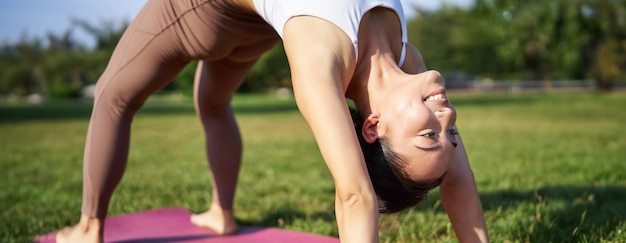 Mujer sonriendo mientras hace asana de puente haciendo yoga en el parque en un tapete de goma