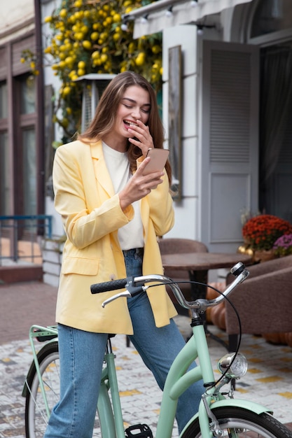 Foto gratuita mujer sonriendo mientras mira smartphone y sentado en bicicleta