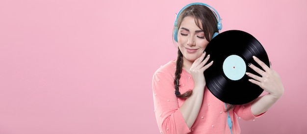 Mujer sonriendo mientras sostiene un disco de vinilo y usa auriculares