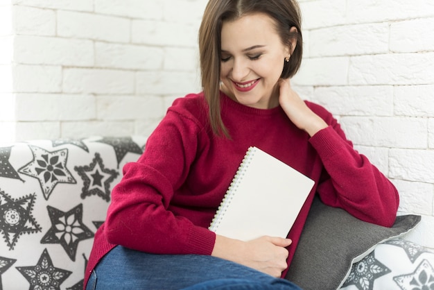 Mujer sonriendo en sofa con libro en la mano