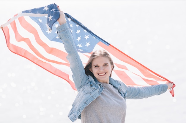 Mujer sonriendo y sosteniendo la bandera estadounidense alto en el cielo