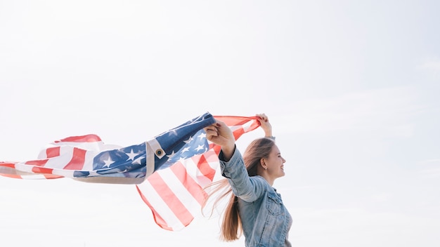 Mujer sonriendo y sosteniendo una bandera estadounidense ancha y alta en el cielo