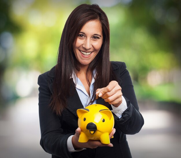 Mujer sonriendo con traje y echando una moneda a una hucha