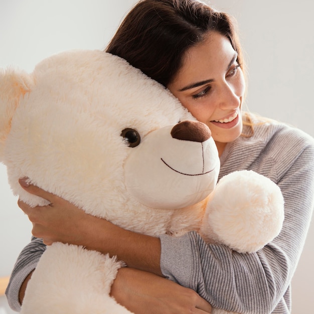 Mujer sonriente abrazando gran oso de peluche en casa