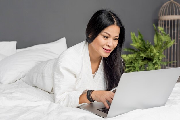 Mujer sonriente acostada en la cama con laptop