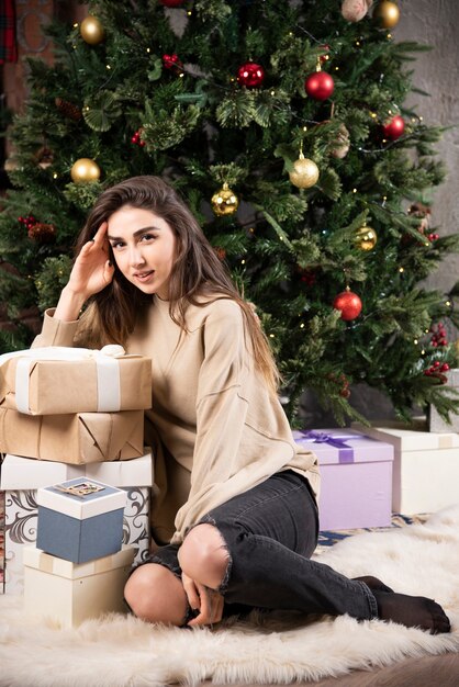 Mujer sonriente acostada sobre una alfombra mullida con regalos de Navidad.