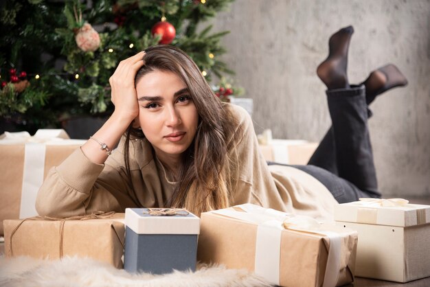 Mujer sonriente acostada sobre una alfombra mullida con regalos de Navidad.