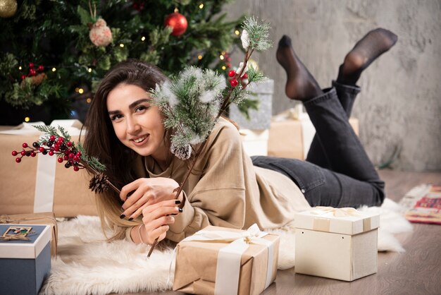 Mujer sonriente acostada sobre una alfombra mullida con regalos de Navidad.