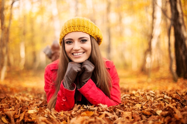 Mujer sonriente acostada sobre hojas de otoño