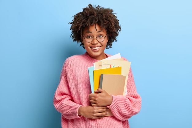 Mujer sonriente con un afro posando en un suéter rosa